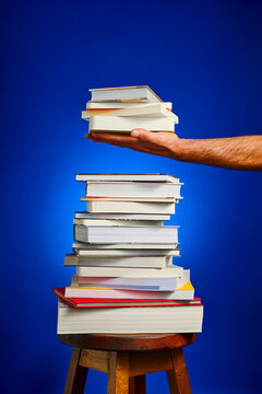Close-up of a collection of books stacked on a wooden stool, against a blue background.