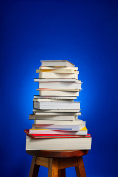 Close-up of a collection of books stacked on a wooden stool, against a blue background.