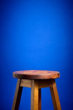 Close-up of an old, empty wooden stool against a blue background.