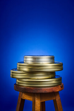 Close-up of a collection of analog film canisters on a wooden stool, against a blue background.