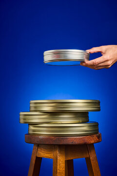 Close-up of a collection of analog film canisters on a wooden stool, against a blue background.