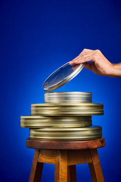 Close-up of a collection of analog film canisters on a wooden stool, against a blue background.