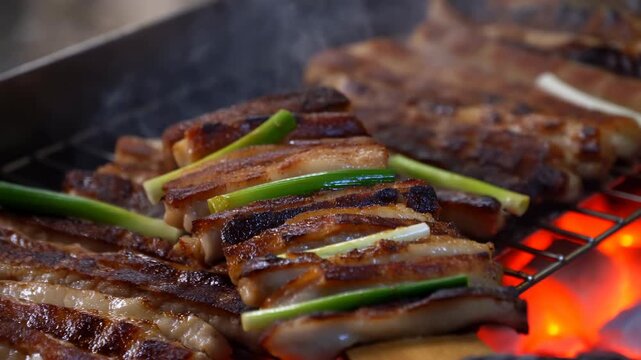 Grilled meat slices with green onion move on wooden spatula over glowing charcoal, showing browned edges, glossy fat, and rising smoke in close view of barbecue grill