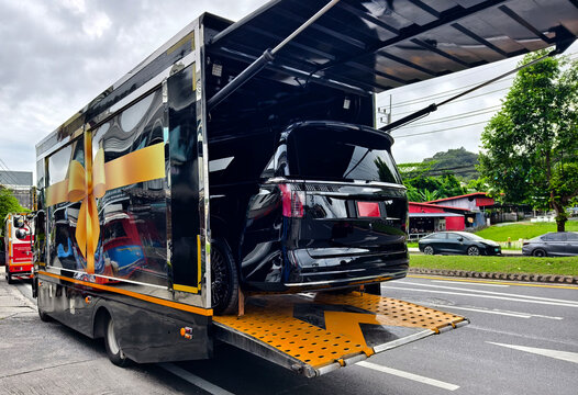 Black SUV being loaded into enclosed car transport trailer on lowered ramp