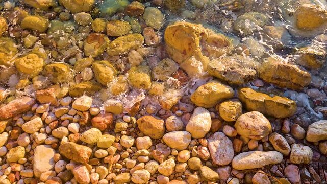 Sea waves splashing over beach coast rocks in golden sunlight