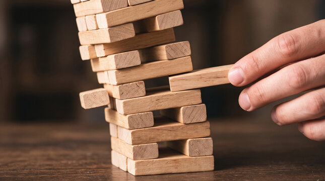 Fingers carefully pulling a wooden block from a tall tower game