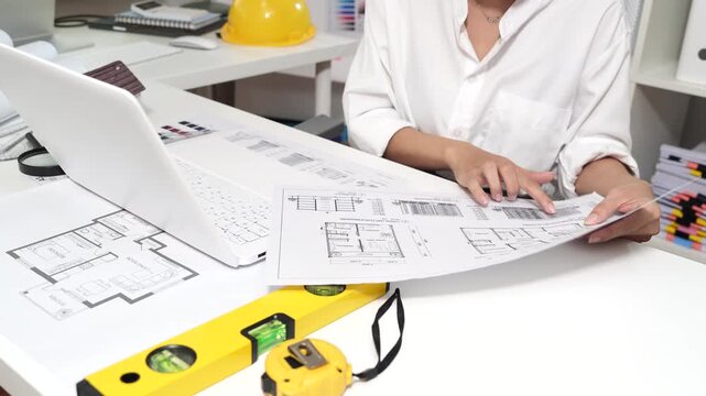 Architect reviewing residential blueprints with a pen and measuring tape, planning house design and construction in a professional workspace with warm natural light.