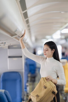 Asian woman opening overhead bin to store hand luggage inside airplane cabin