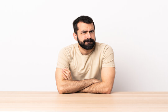 Caucasian man with beard in a table feeling upset.