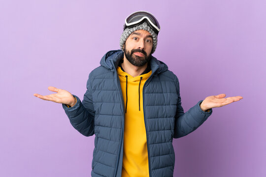 Skier man with snowboarding glasses over isolated purple background having doubts while raising hands