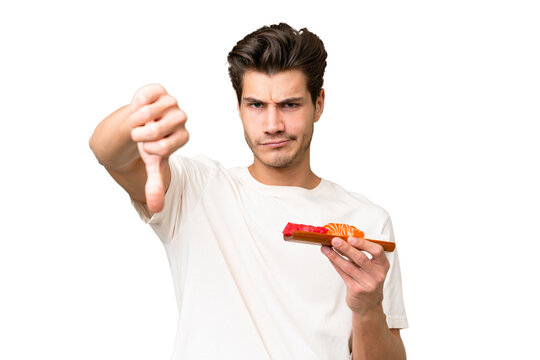 Young caucasian man holding sashimi over isolated background showing thumb down with negative expression