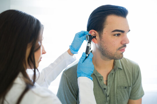 Closeup of a doctor examining male patient's ear with an otoscope during a medical checkup for hearing health