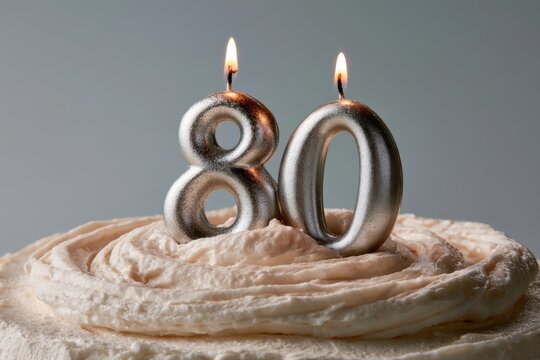 Silver number candles burning atop frosted cake, marking an 80th birthday milestone