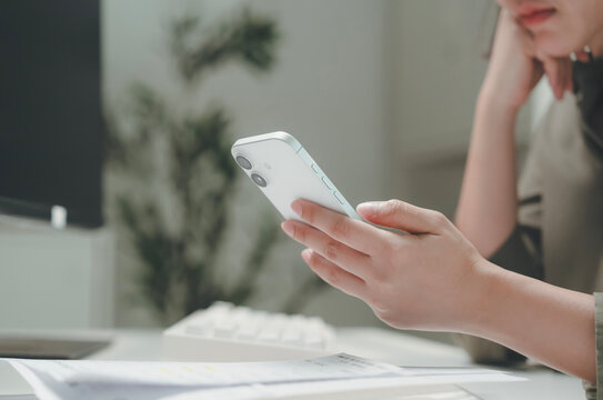 Woman using smartphone at office desk, business communication and mobile technology with computer, calculator and financial documents,online messaging,research and accounting work in office workplace