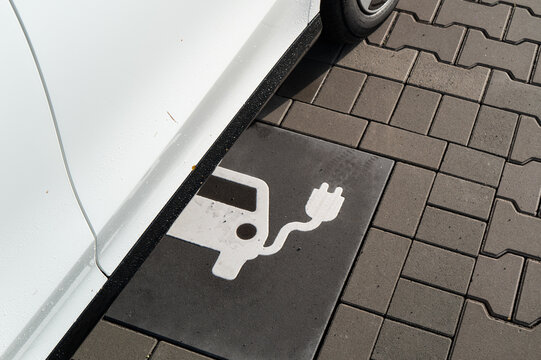 Electric car parked over a marked charging space on a paved street