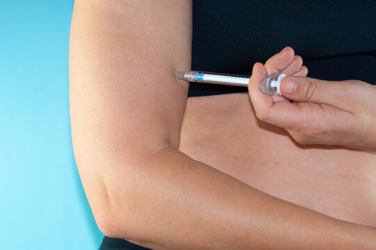 hand injecting syringe into upper arm on blue background, anabolic steroids and doping in bodybuilding, close up of subcutaneous injection with copy space for banner design concept of sports, fitness