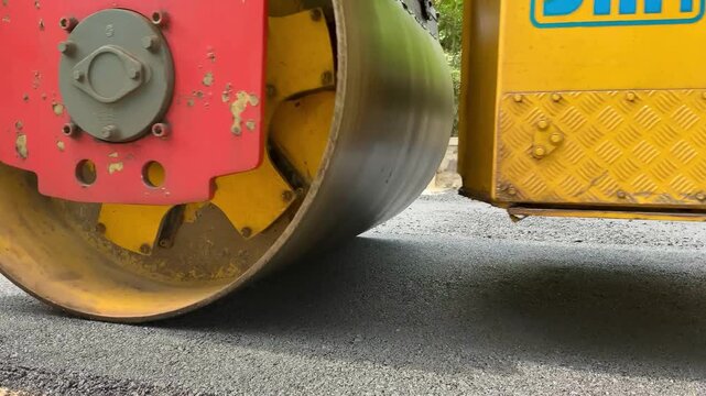 Close-up of a heavy yellow road roller compacting fresh asphalt on a construction site