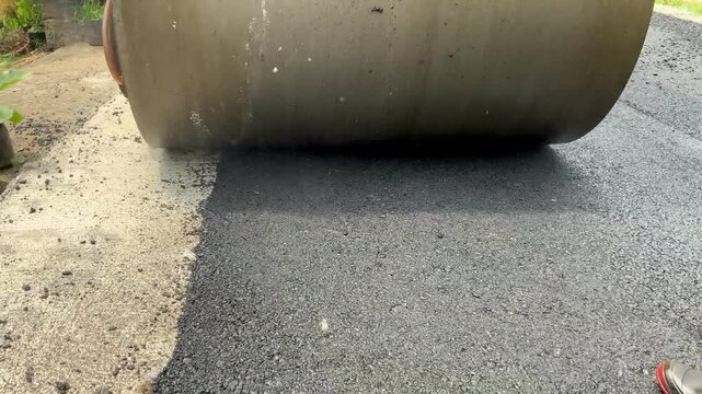Road construction worker using a heavy steamroller to compact fresh asphalt on a new road surface