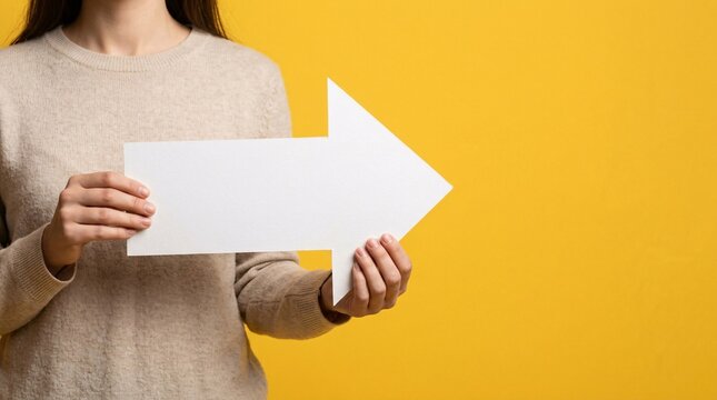 Woman holding blank white arrow sign against bright yellow studio background