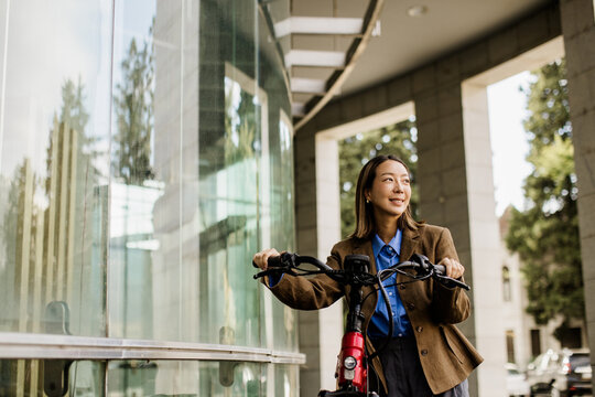 Korean woman pauses with her electric bike by a glass building