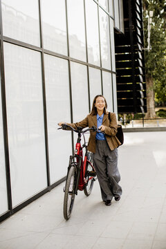 Korean woman guides her electric bike beside a glass facade