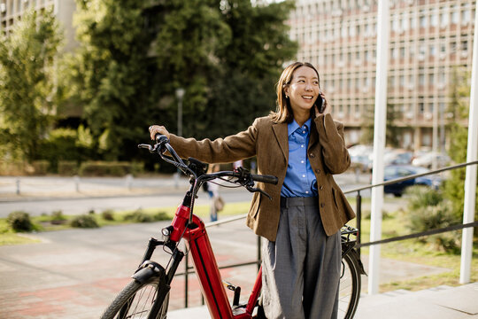 Woman smiling on phone while standing next to her bicycle in urban area
