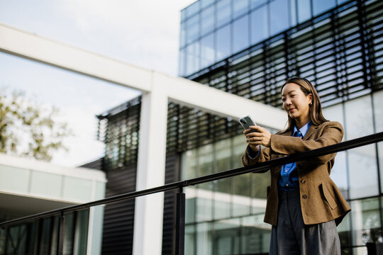 Korean woman smiles while using her smartphone near modern architecture