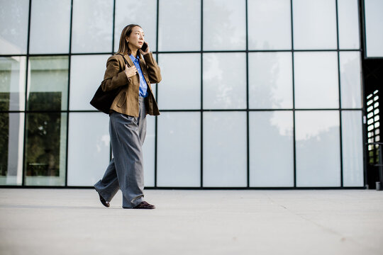 Woman walking and talking on a phone outside a modern building