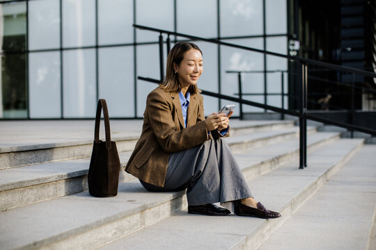 Woman sitting on stairs using mobile phone in urban area during daytime