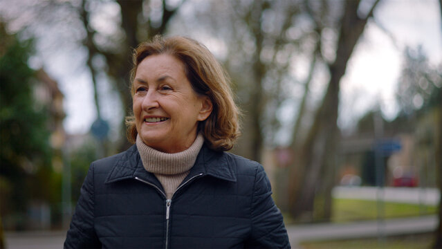 Joyful Caucasian senior woman laughing while walking in the park, carefree happiness and zest for life
