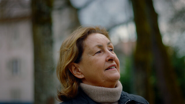 Profile of a Caucasian older woman looking around outdoors with a soft smile, calm confidence and grace