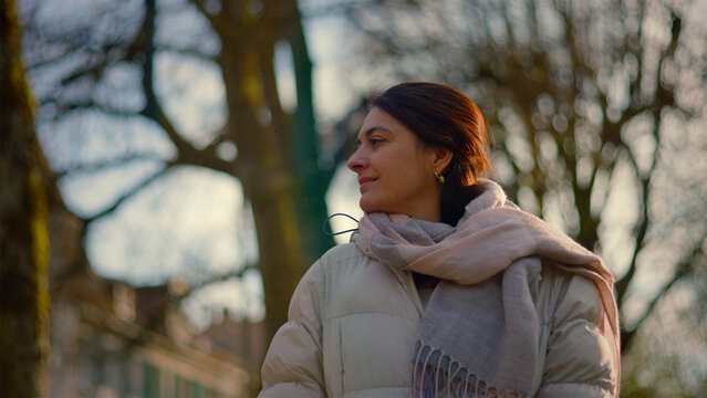 Serene Caucasian woman looking up at bare trees at golden hour, peace, gratitude and connection to nature