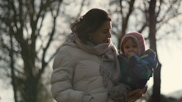 Caucasian mother holding her baby outdoors in winter under bare trees, love, protection and family bond