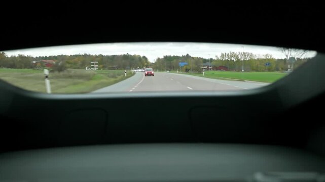 Close-up view of traffic on rural road through rear window of moving car. Sweden.
