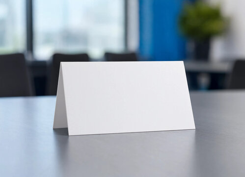 Blank white paper table tent sign mockup sitting on a dark grey conference room table
