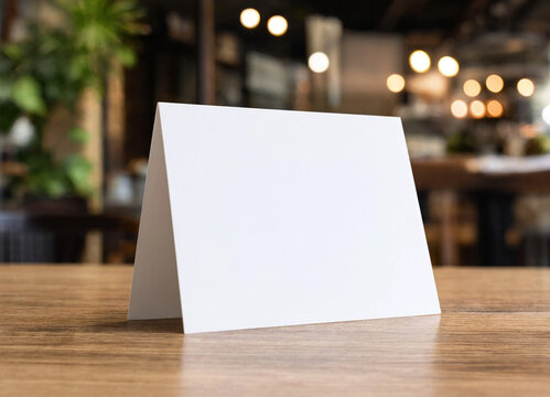 Blank white paper table tent standing on a wooden surface inside a cafe