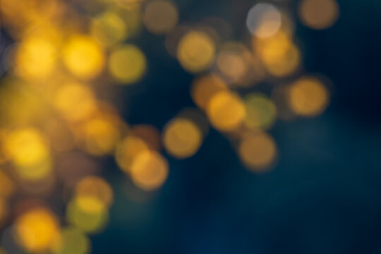 Abstract autumn background with blurred golden yellow birch leaves, warm amber bokeh lights and deep blue tones, creating a soft seasonal nature backdrop with copy space.