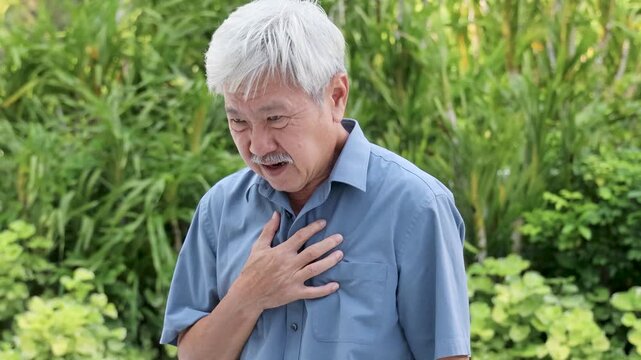elderly southeast asian man in his 60s with white hair, experiencing acid reflux and chest pain outdoors in daylight, showing discomfort