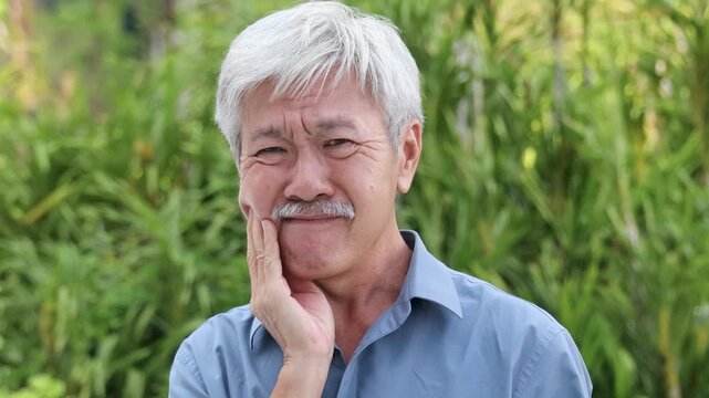 Old asian senior man with crooked teeth suffering from toothache, tooth decay, tooth sensitivity, teeth grinding problem, concept image for oral health care or dental care