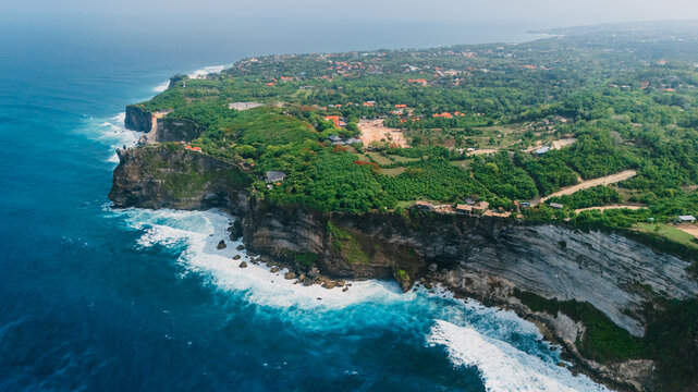 Drone view of coastline with rocky cliffs, ocean with waves in Uluwatu, Bali