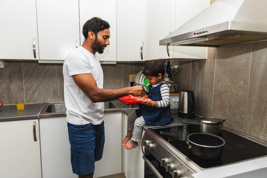 Indian Father Feeding Toddler Daughter on Modern Kitchen Counter
