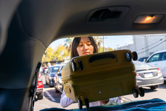 traveler putting suitcase into trunk of car