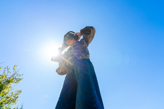 woman putting on headphones listening to music outside blue sky