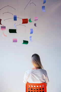 Woman Sitting on Chair Under Colorful Hanging Artwork
