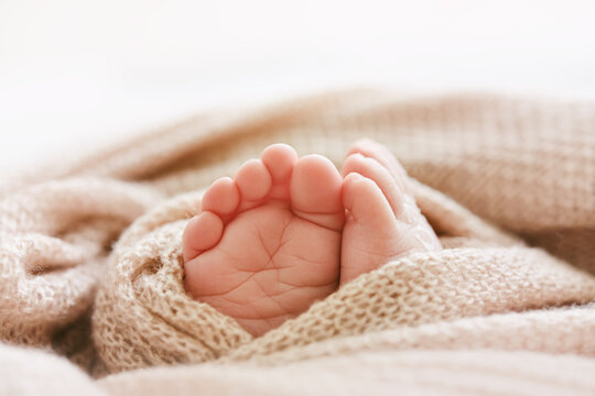 Tiny newborn feet and toe peeking out of a soft pink knit baby blanket