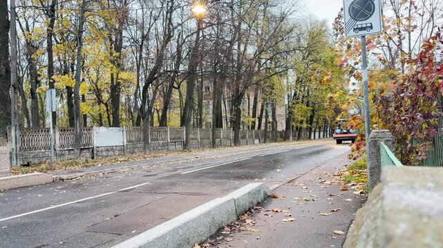 A tractor drives quickly down a quiet street lined with colorful autumn trees. The motion creates a lively contrast in the peaceful atmosphere of Pushkin, Russia.