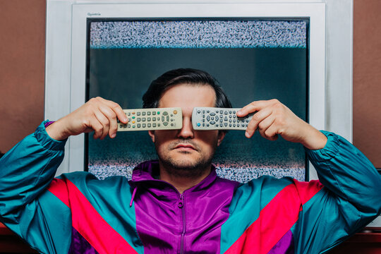 Retro man covering face with two TV remotes, static television screen behind