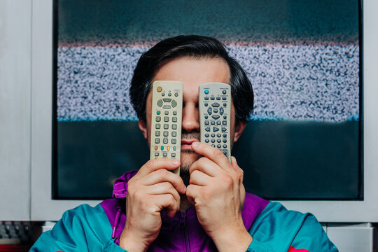 Retro man covering face with two TV remotes, static television screen behind