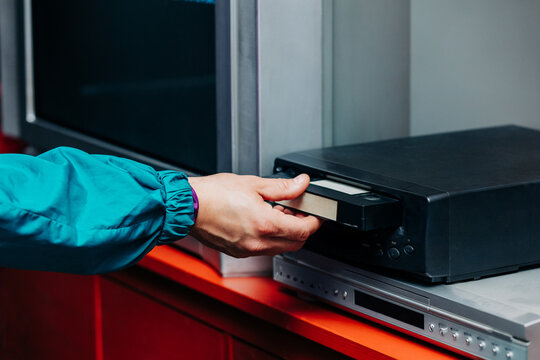 Hand in neon sleeve inserting VHS tape into vintage player
