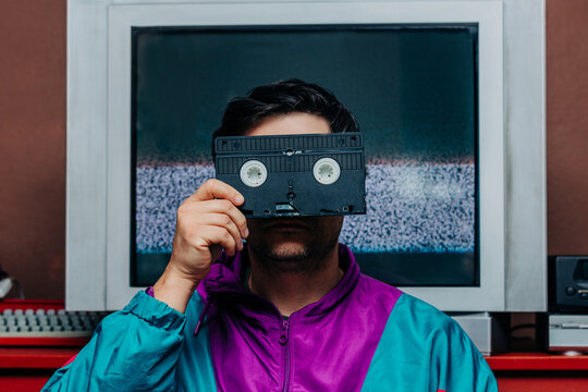 Man in retro 80s jacket holding VHS tape over face, TV static backgroun